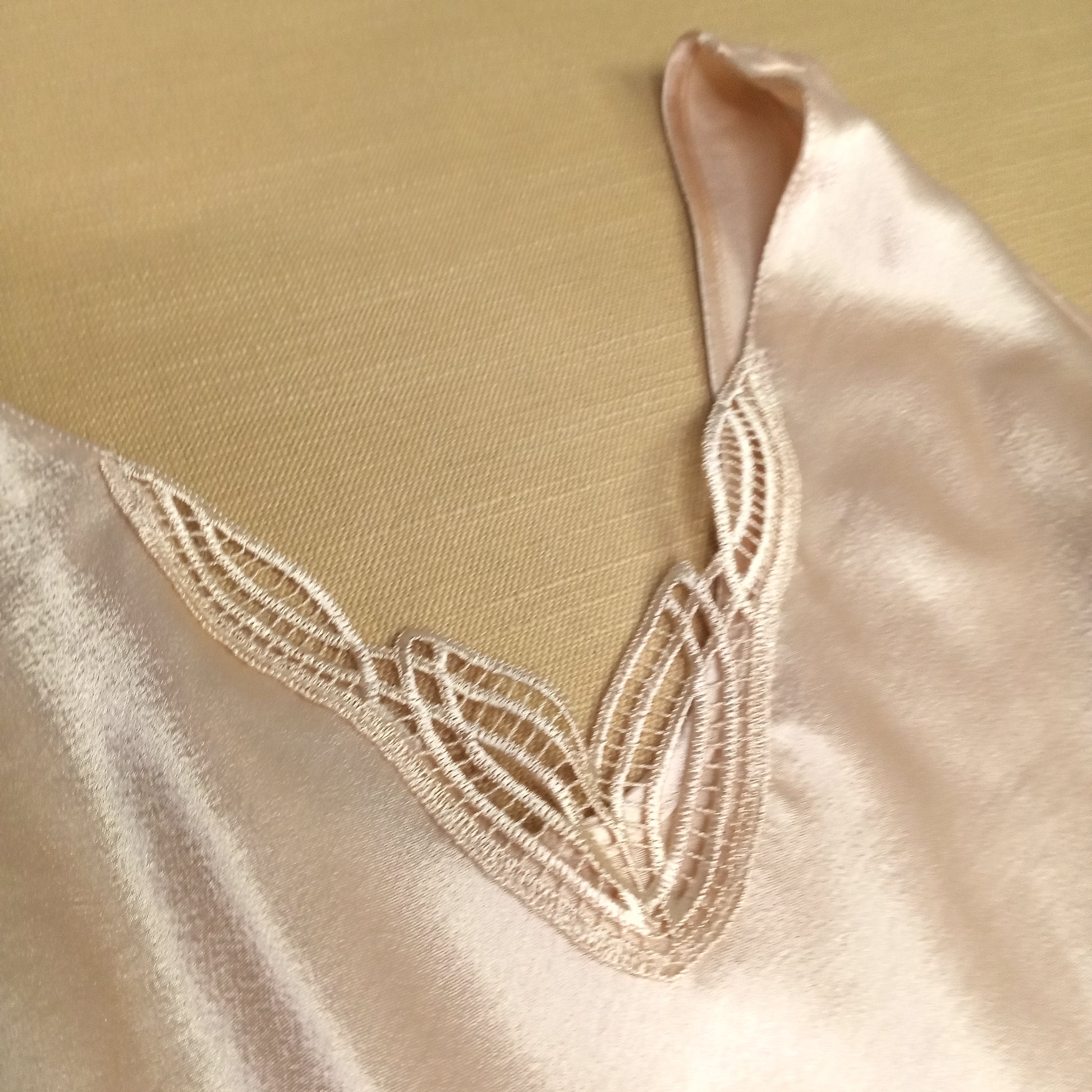 Close-up of a beige tank top with intricate lace detailing on a beige background