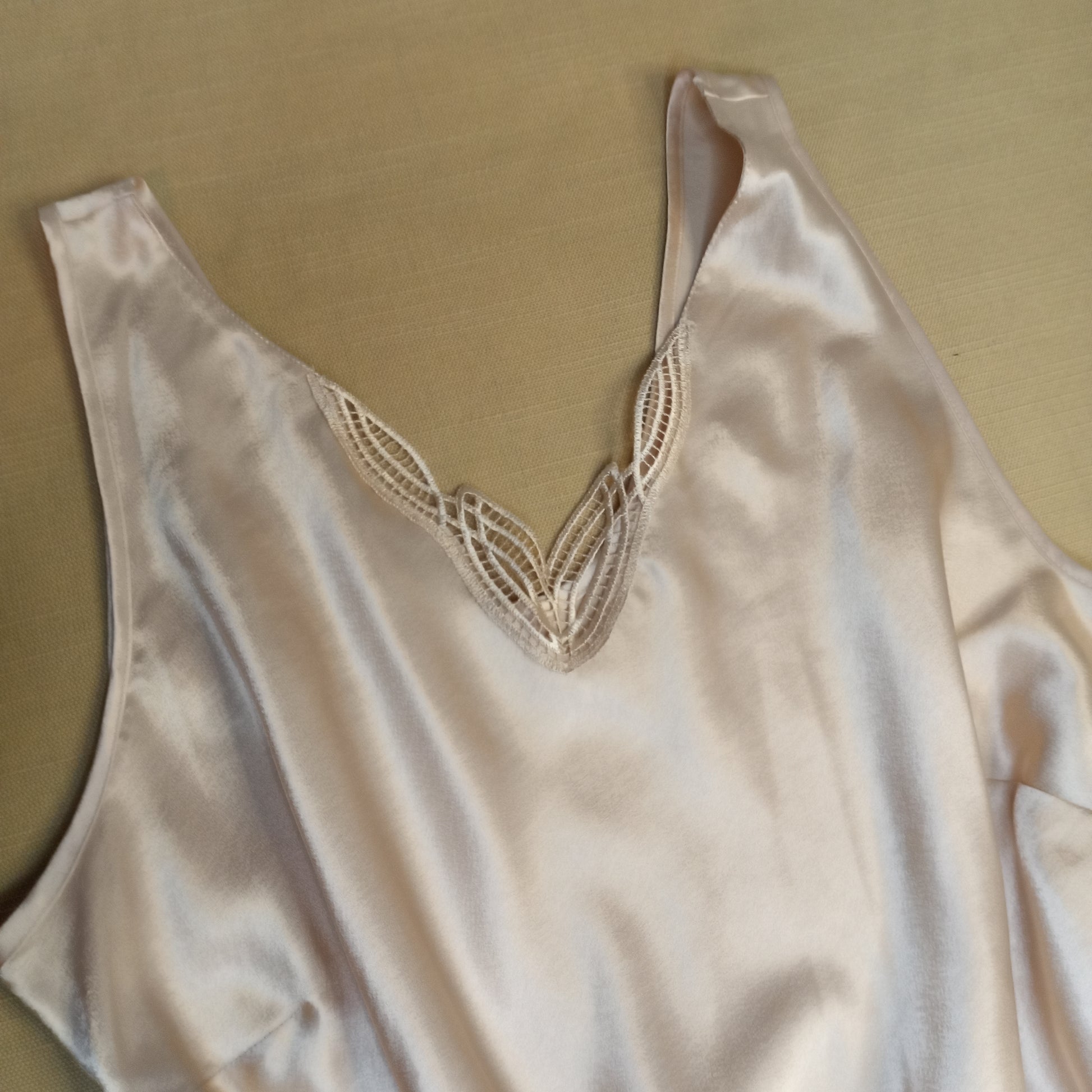 Silky nude tank top with lace detailing on a beige background