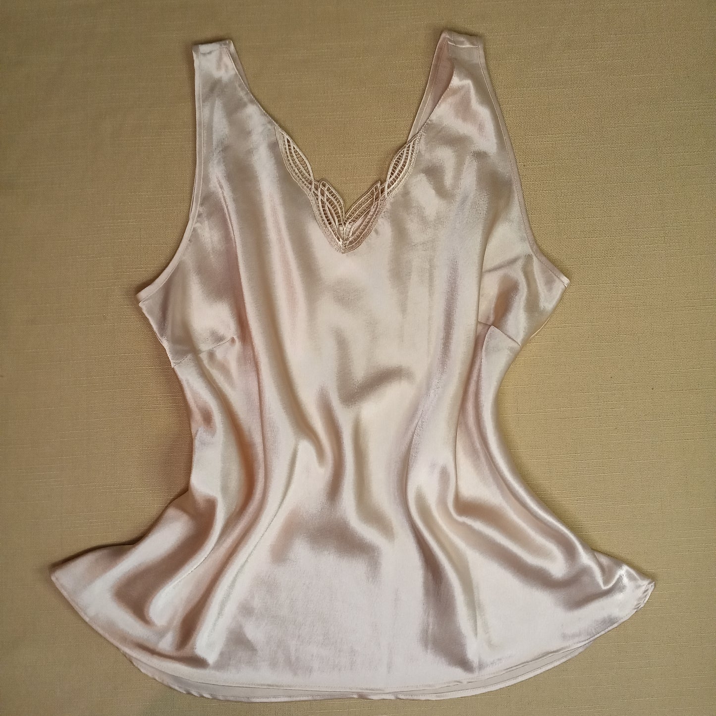 Silky nude tank top with lace details on a beige background